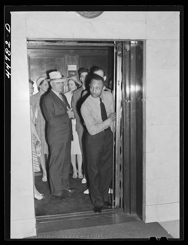 Elevator operator working a manual car with passengers, Barr Building, Washington DC, 1941